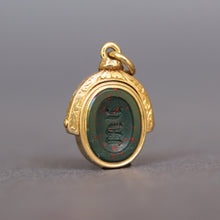 Load image into Gallery viewer, Antique bloodstone spinner fob pendant with intaglio depicting and knight's armored arm rising from the water holding an anchor. The monogram initials on the other side are MJ. Has a gold frame engraved and made from 18ct gold.
