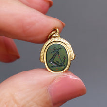 Load image into Gallery viewer, Antique bloodstone spinner fob pendant with intaglio depicting and knight's armored arm rising from the water holding an anchor. The monogram initials on the other side are MJ. Has a gold frame engraved and made from 18ct gold.

