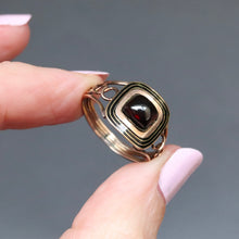 Load image into Gallery viewer, A rectangular antique Georgian mourning memorial ring featuring a dark red garnet cabochon cut in a gold setting with concentric gold bands.
